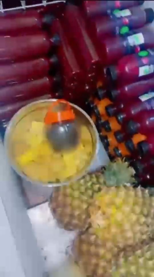 Fresh pineapple being prepared beside crates of finished Uzzy juice bottles